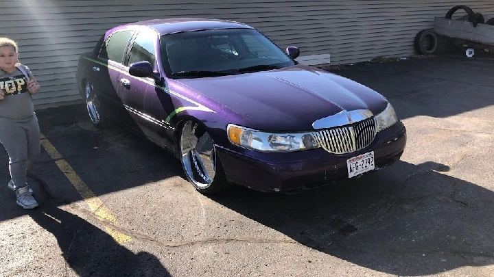 Purple car parked outside, child nearby. Junk car yard.