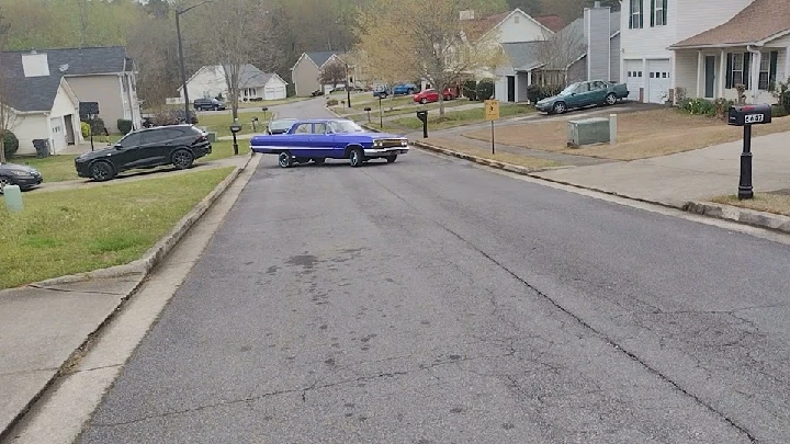 Purple car on residential street with houses.