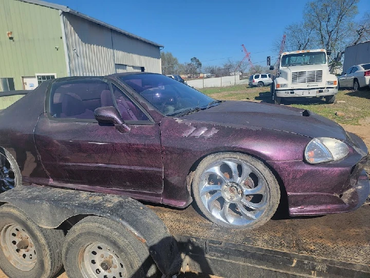 Purple car on a trailer under clear blue sky.