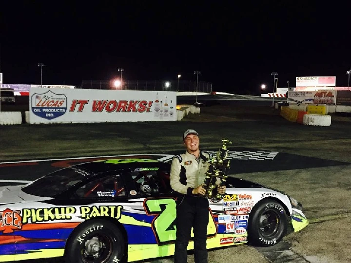 Racer holding a trophy next to a colorful car.