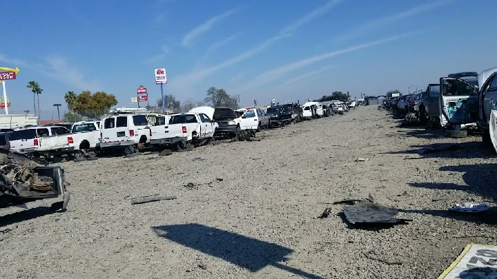 Row of vehicles in a junkyard under a clear sky.