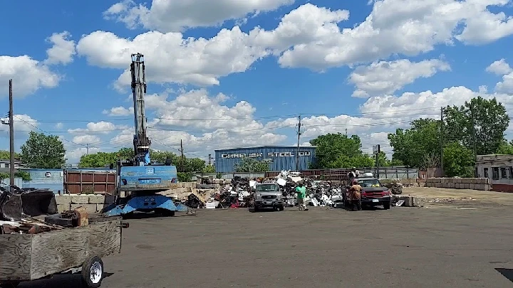 Scrapyard with machinery and vehicles under a blue sky.