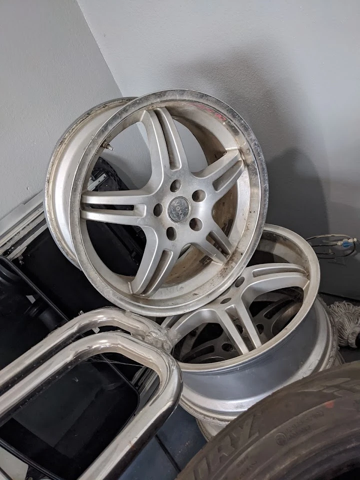 Stack of used car wheels and rims for sale.