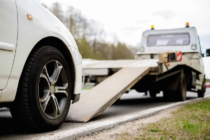 Tow truck loading a car on a roadside ramp.