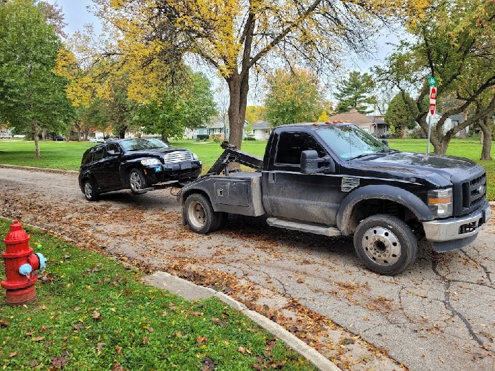 Tow truck retrieving a car on a tree-lined street.