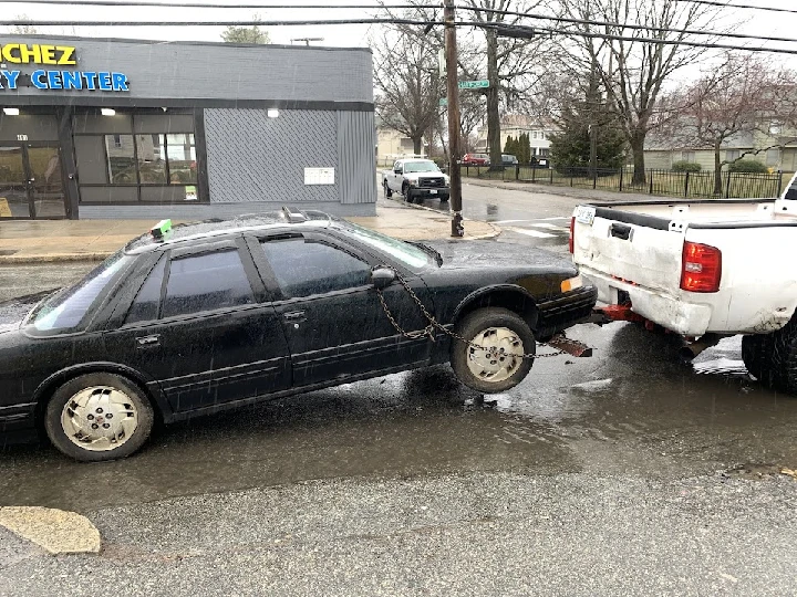 Towing an old car in a rainy urban setting.