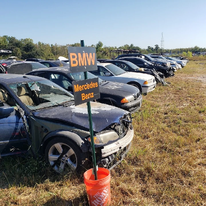 Used cars in a salvage yard with brand signs.