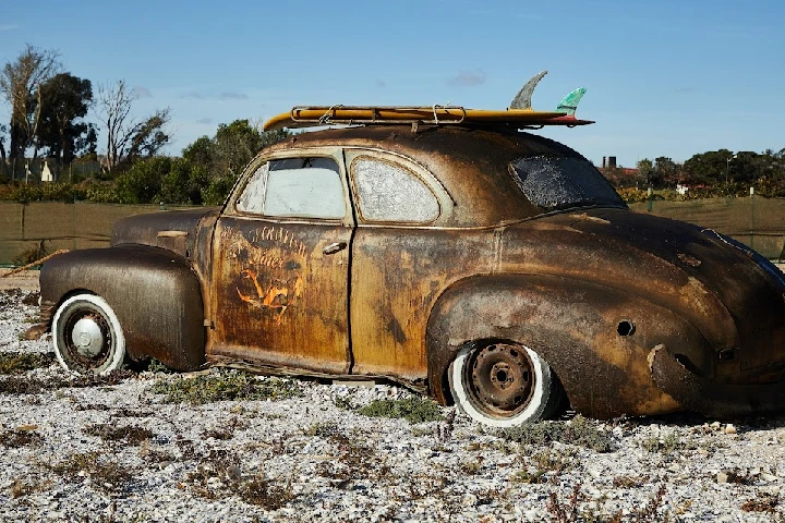 Vintage rusty car with surfboards on top.