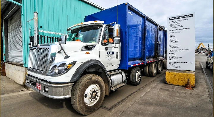 White truck with blue container at scrap yard.