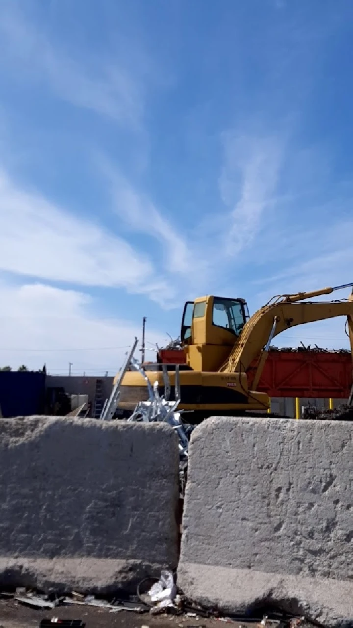 Yellow excavator at a recycling facility under blue sky.