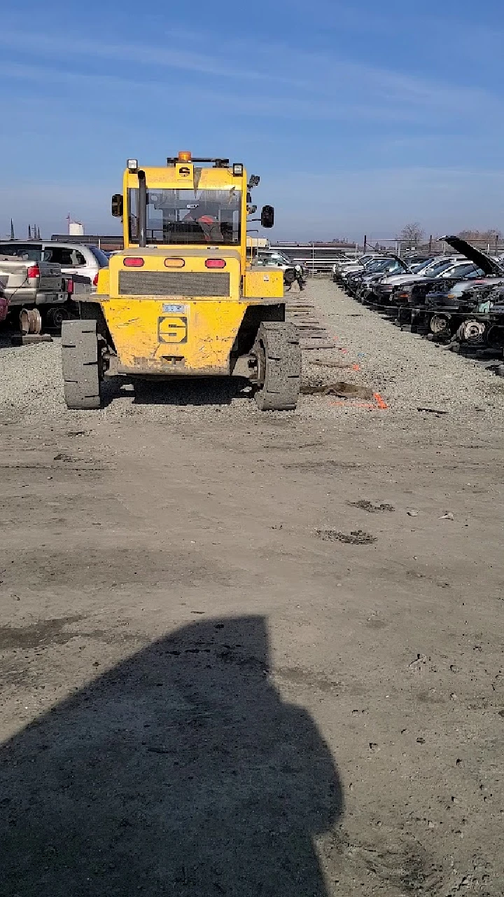 Yellow machinery in a salvage yard with cars.