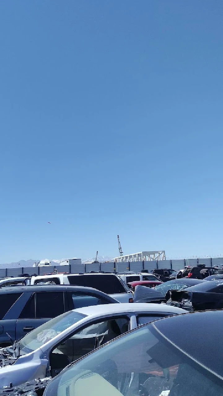 Auto recycling yard with stacked vehicles and blue sky.