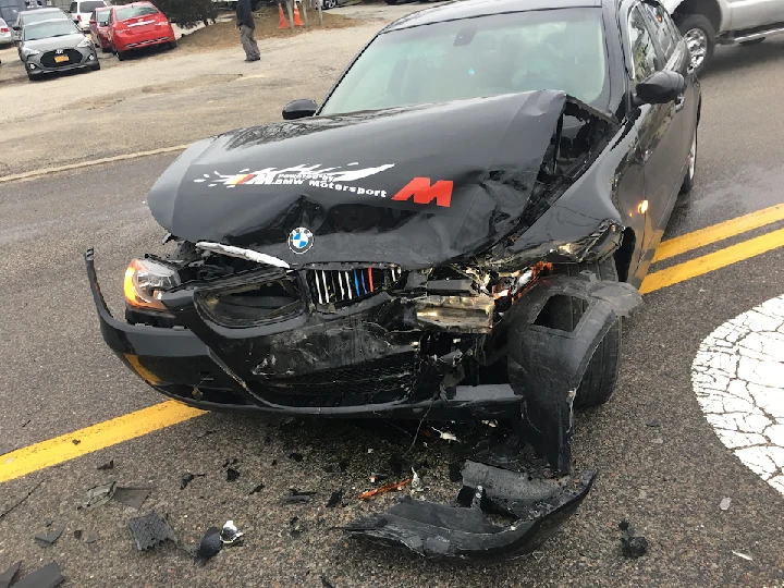 Damaged black BMW after a collision on the road.