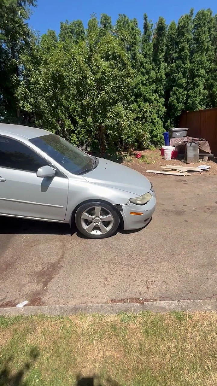 Damaged silver car parked on a sunny street.