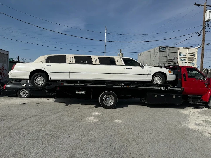 White limousine being towed on a flatbed truck.